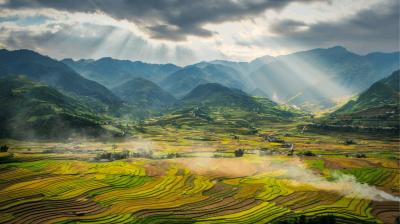 Sunlight streams through clouds over terraced rice fields and green mountains, creating a patchwork landscape in a rural valley.